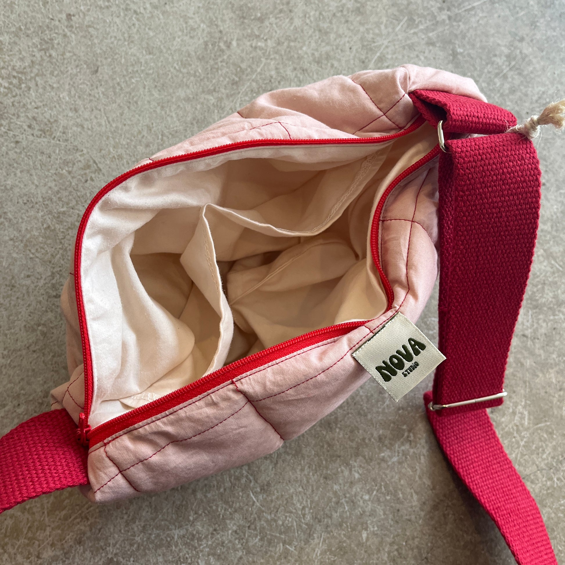 Pink bag with red strap and visible 'NOVA' tag on a gray surface