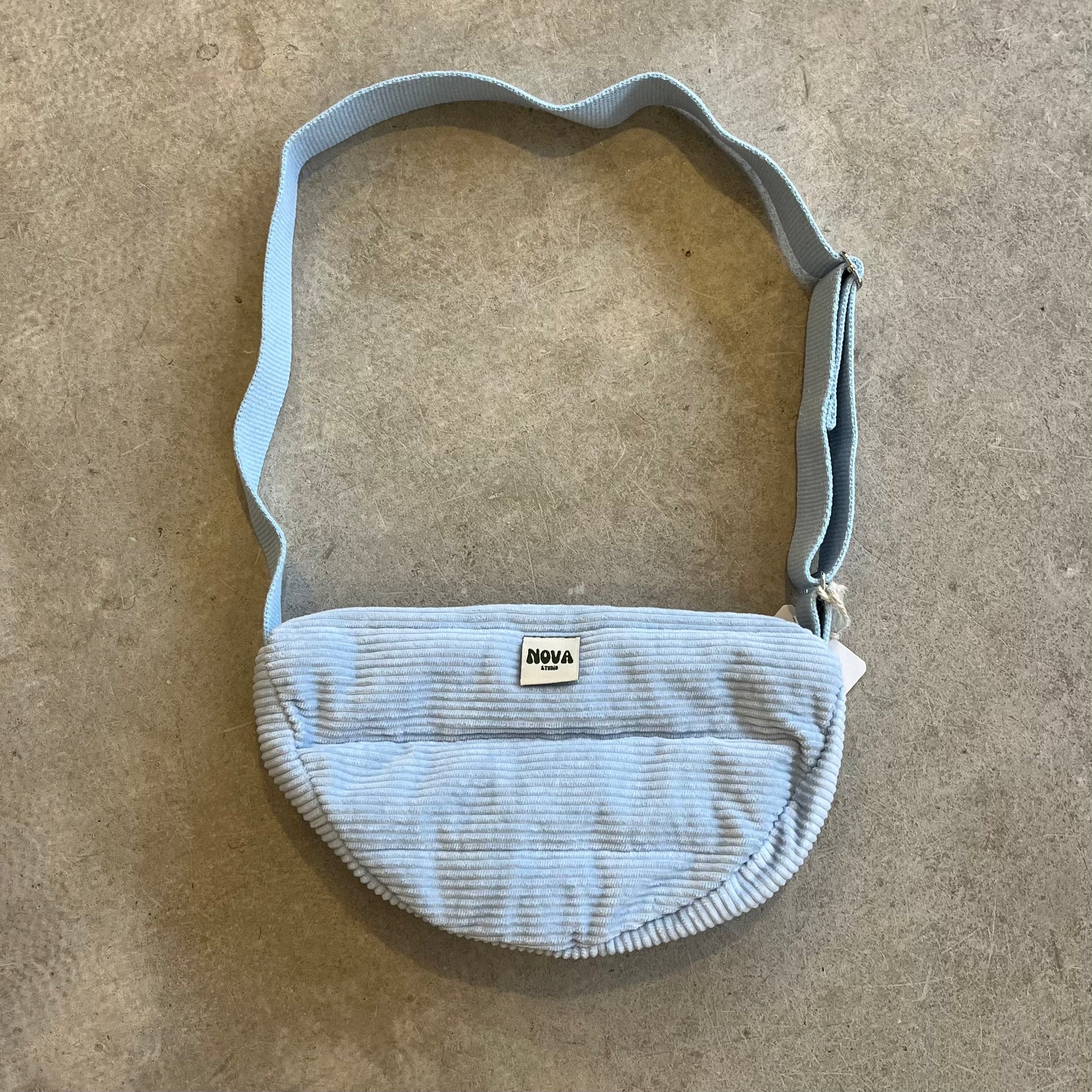 Light blue corduroy waist bag on a beige surface