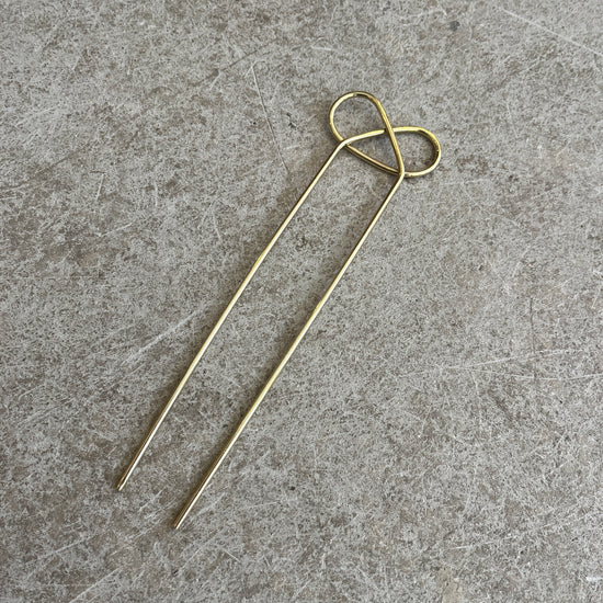 a pretzel shaped brass hairpin on a concrete background