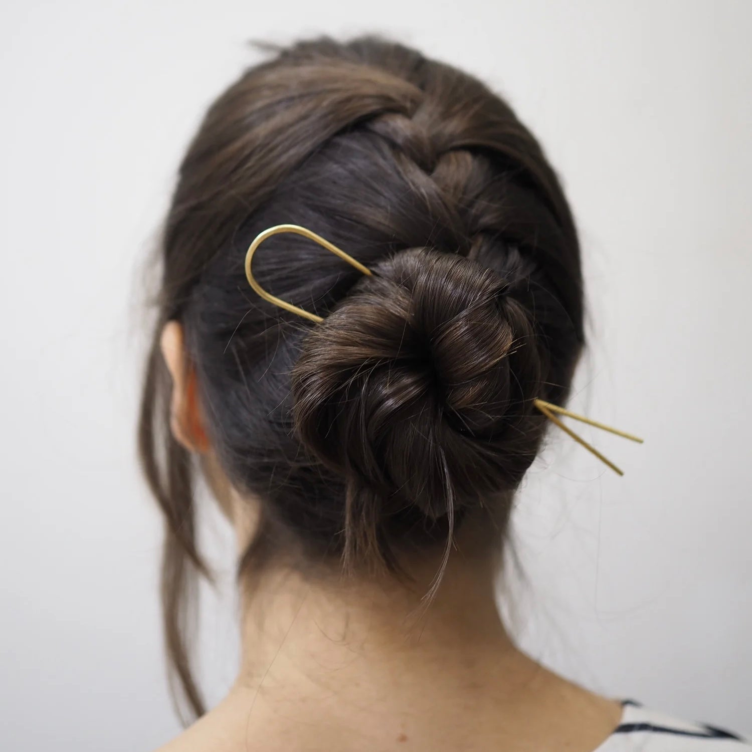 Person with a bun hairstyle using gold hair pin on a plain background
