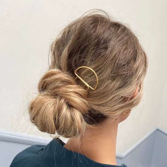 Person with blonde hair styled in a bun with a gold hair pin against a neutral background