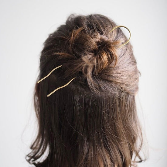 Person with hair styled in a bun using gold coloured  hair pin on a white background