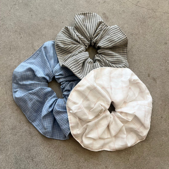 Three checkered scrunchies in blue, white, and gray on a beige surface