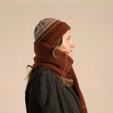 Person wearing a brown knitted hat and scarf on a beige background