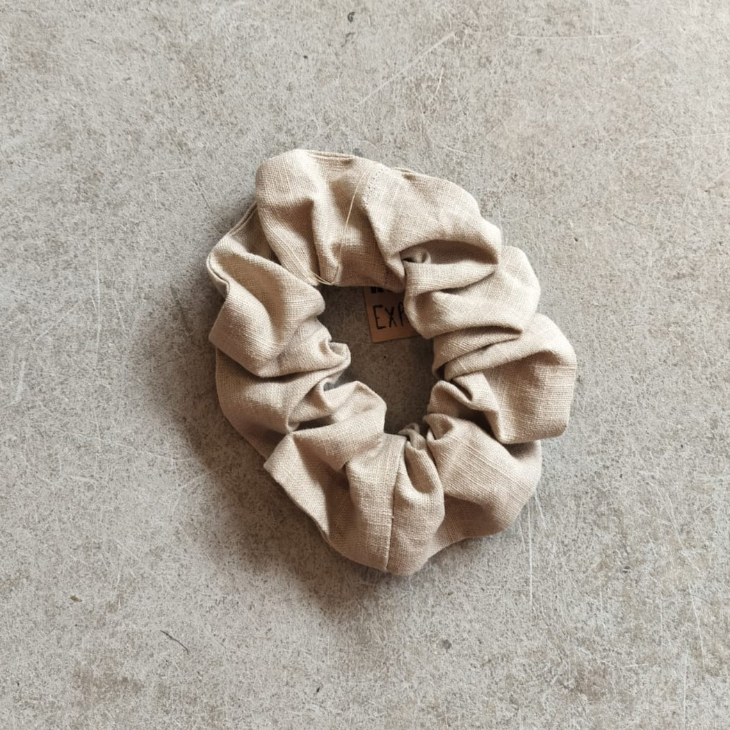 A taupe colored bio linen scrunchie on a textured background.