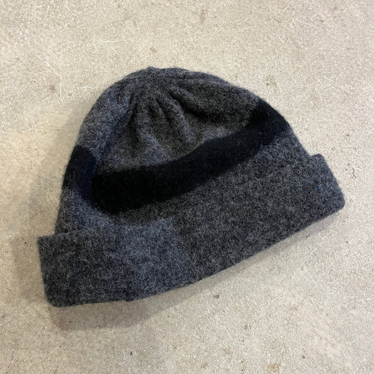 Grey beanie with black stripe on a concrete surface