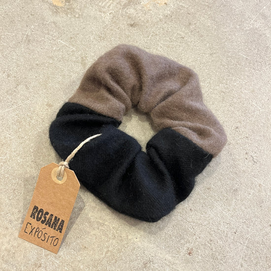 Two-tone black and brown scrunchie with a tag on a concrete background