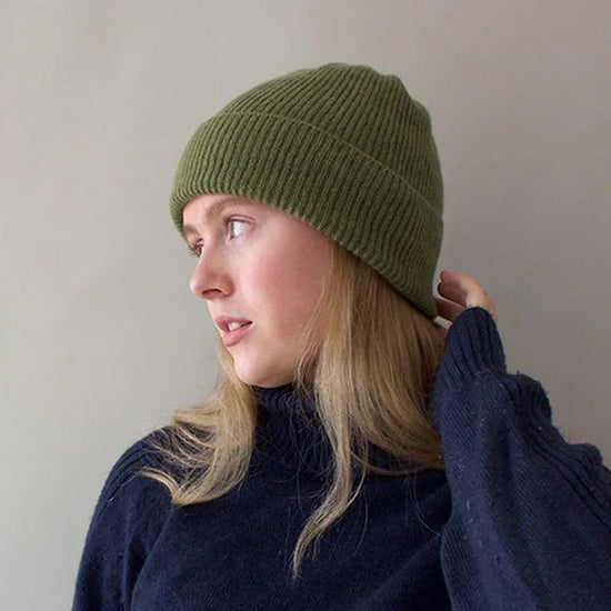 Person wearing a green knit beanie and navy sweater against a plain background