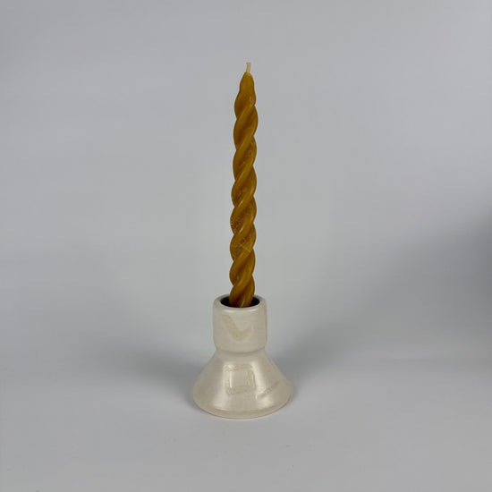 Twisted candle in a white holder on a gray background