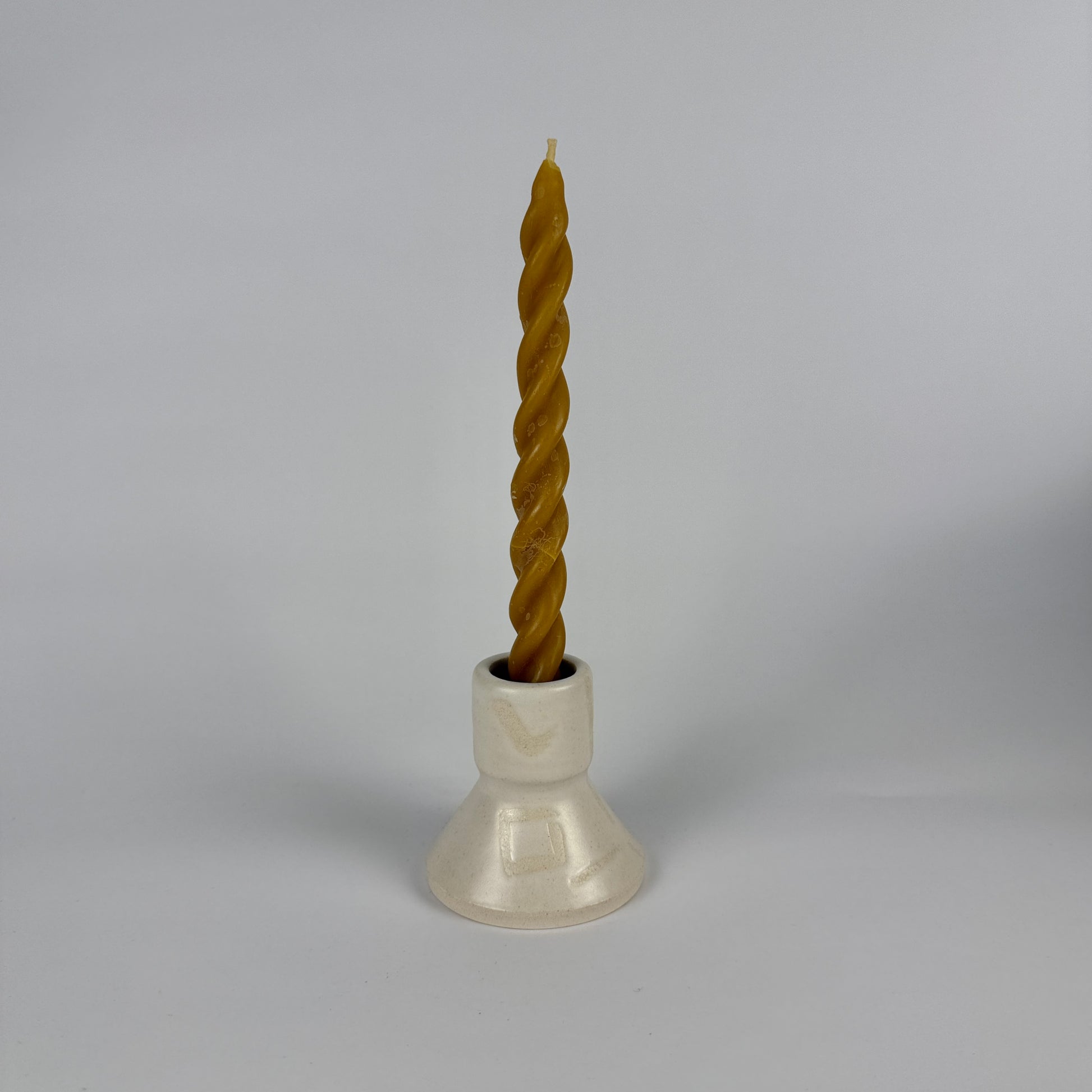 Twisted candle in a white holder on a gray background
