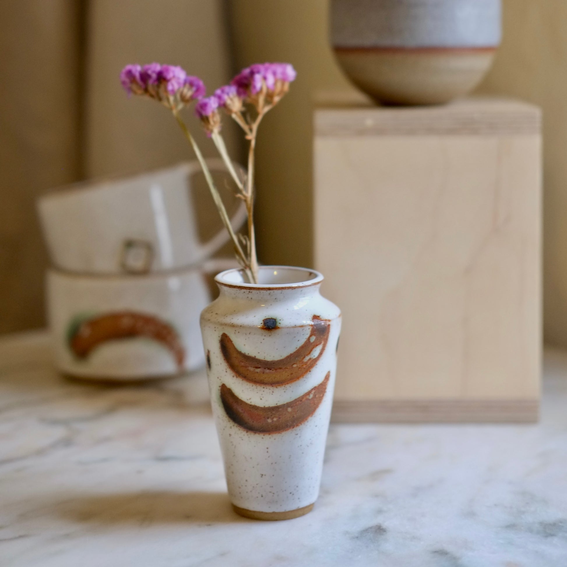 Ceramic vase with decorative design on a marble surface, featuring a small bouquet of purple flowers.