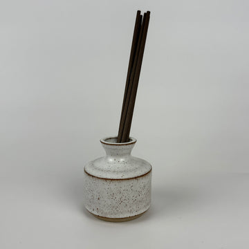 Ceramic diffuser bottle with black sticks on a gray background