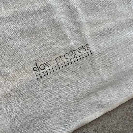 Text 'slow progress' printed on a textured gray fabric surface