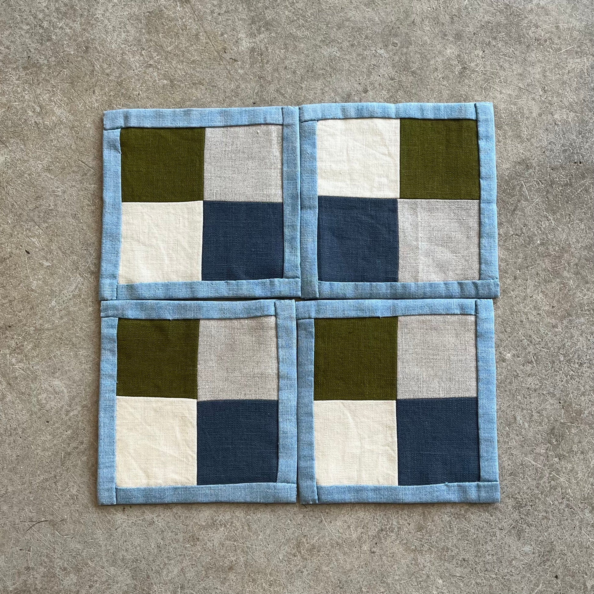 Fabric patchwork square with green, blue, and white squares on a concrete surface