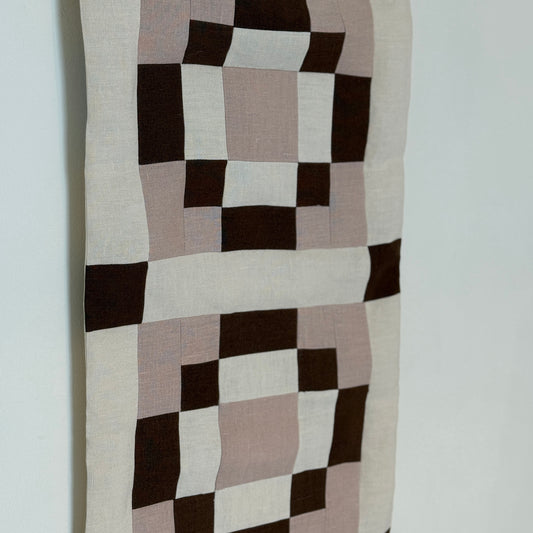 Checkered fabric wall hanging with brown, beige, and black squares on a white background