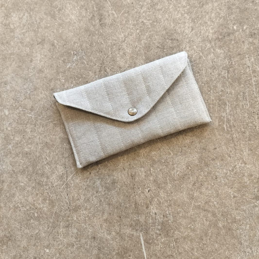 A collection of quilted pouches in beige, green, blue, and brown colors, arranged one inside the other on a textured background.