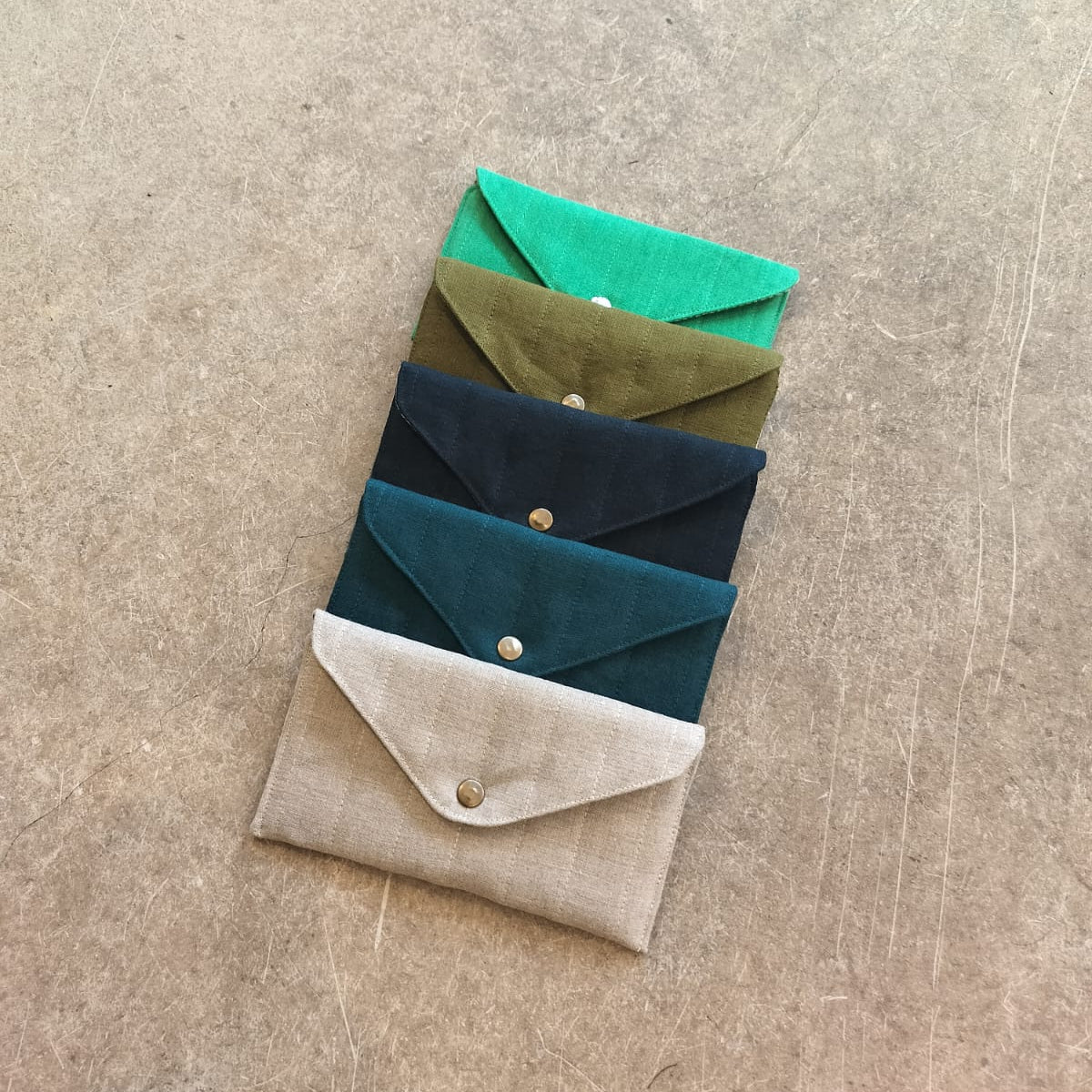 A collection of quilted pouches in beige, green, blue, and brown colors, arranged one inside the other on a textured background.