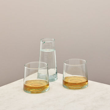 Two glasses filled with whiskey and jug filled with water on a taupe background