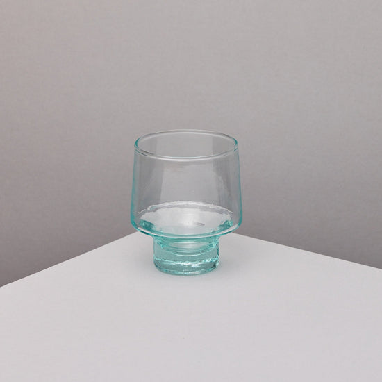 A clear wine glass on a plinth in front of a grey background