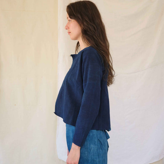Woman wearing a blue top and jeans against a plain background