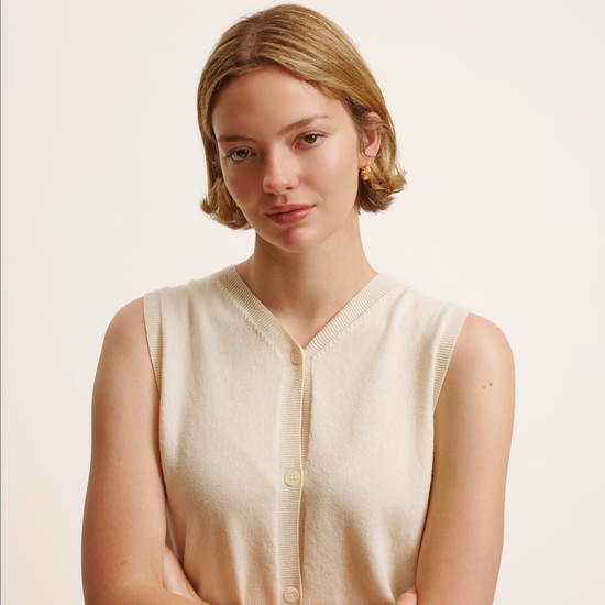 Woman wearing a beige sleeveless cardigan against a plain background