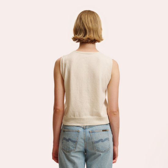 Person wearing a beige sleeveless top and blue jeans on a plain background