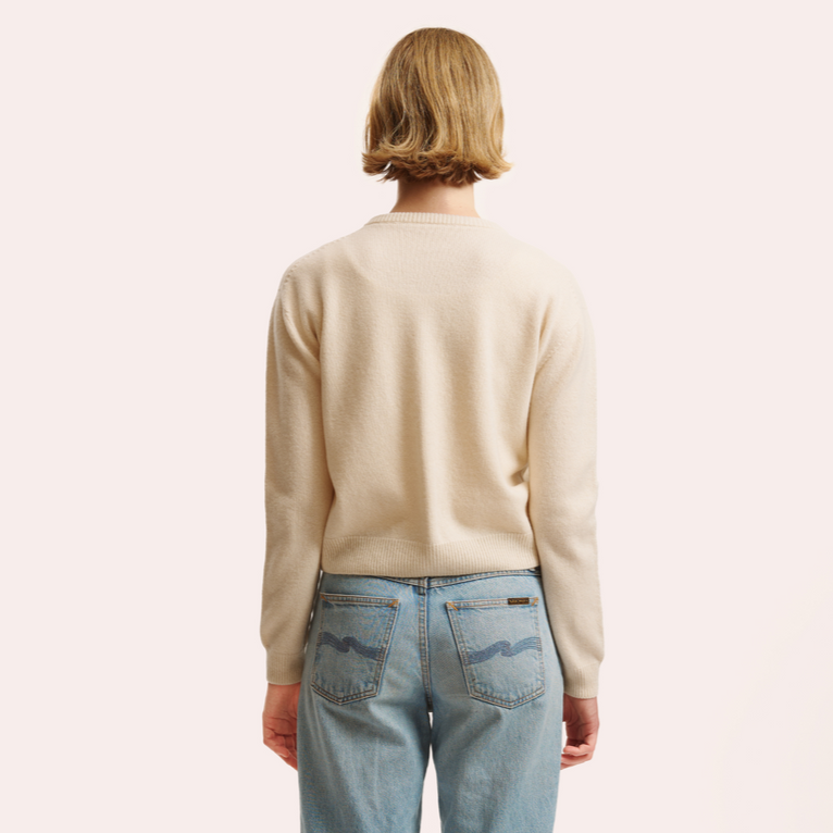 Person wearing a beige sweater and blue jeans on a white background