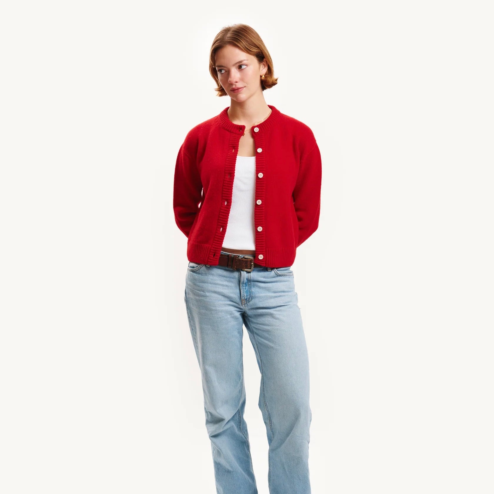 Woman wearing a red cardigan, white shirt, and light blue jeans on a white background