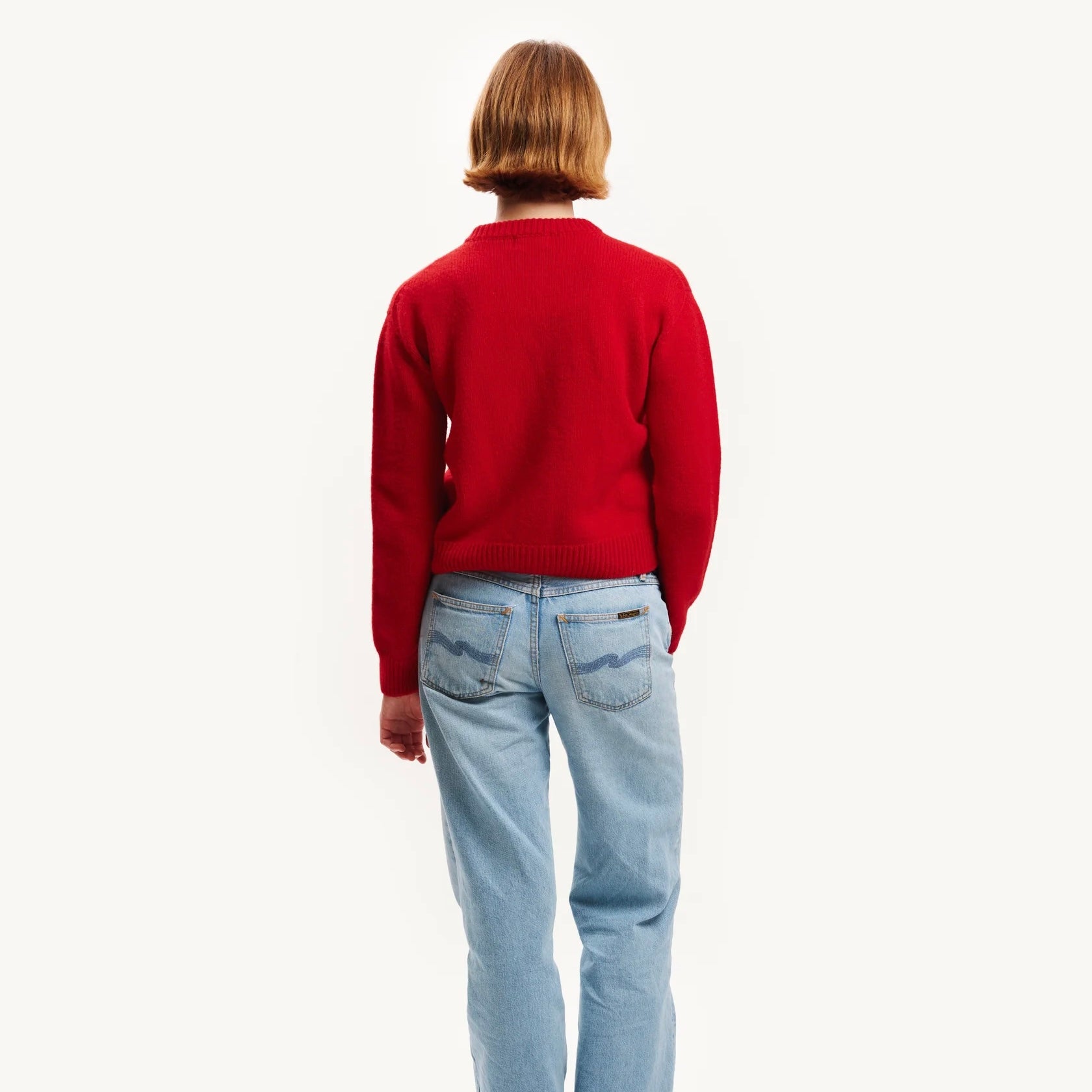 Person wearing a red sweater and light blue jeans on a white background
