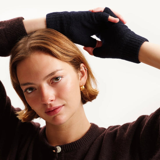Woman wearing a dark sweater and navy fingerless gloves against a white background
