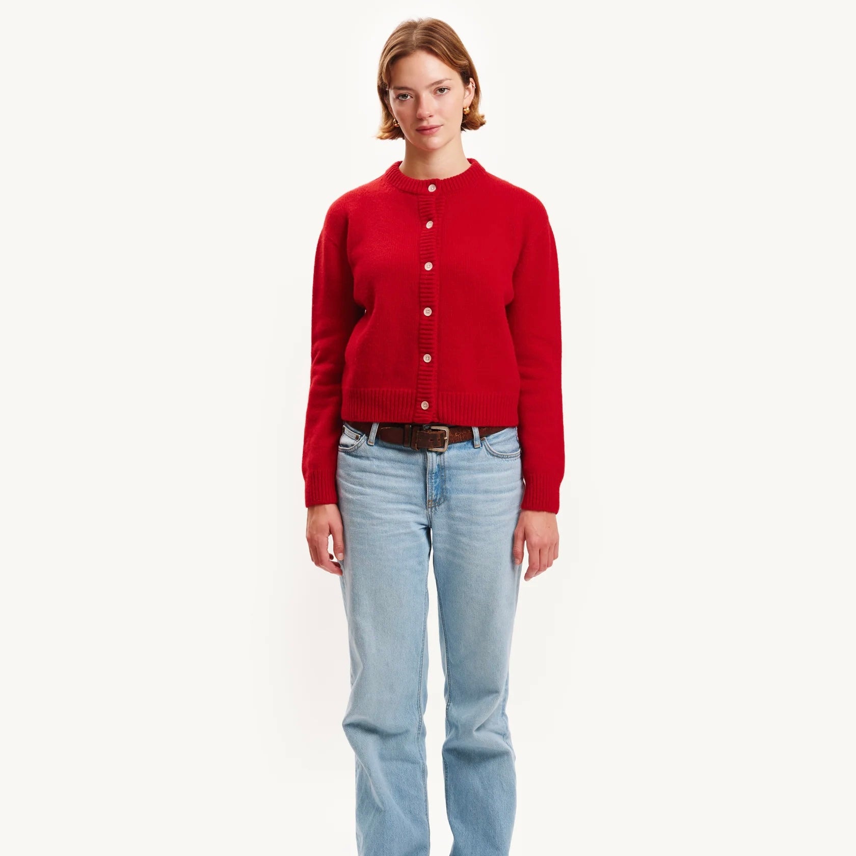 Person wearing a red cardigan and light blue jeans on a white background