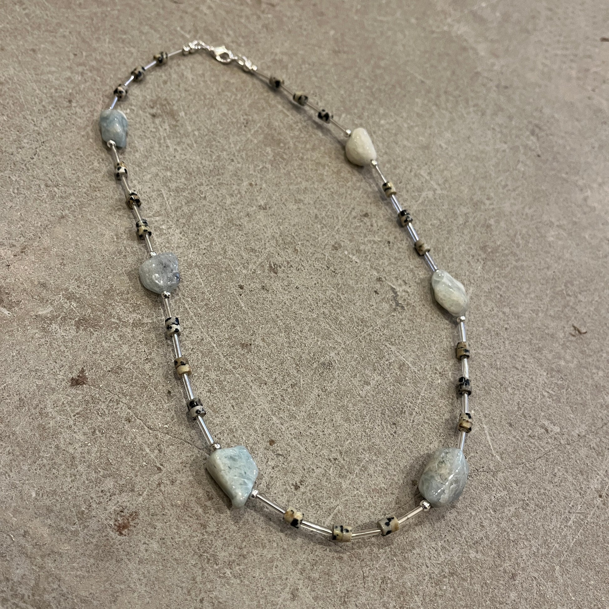 Necklace with blue and speckled beads on a concrete surface