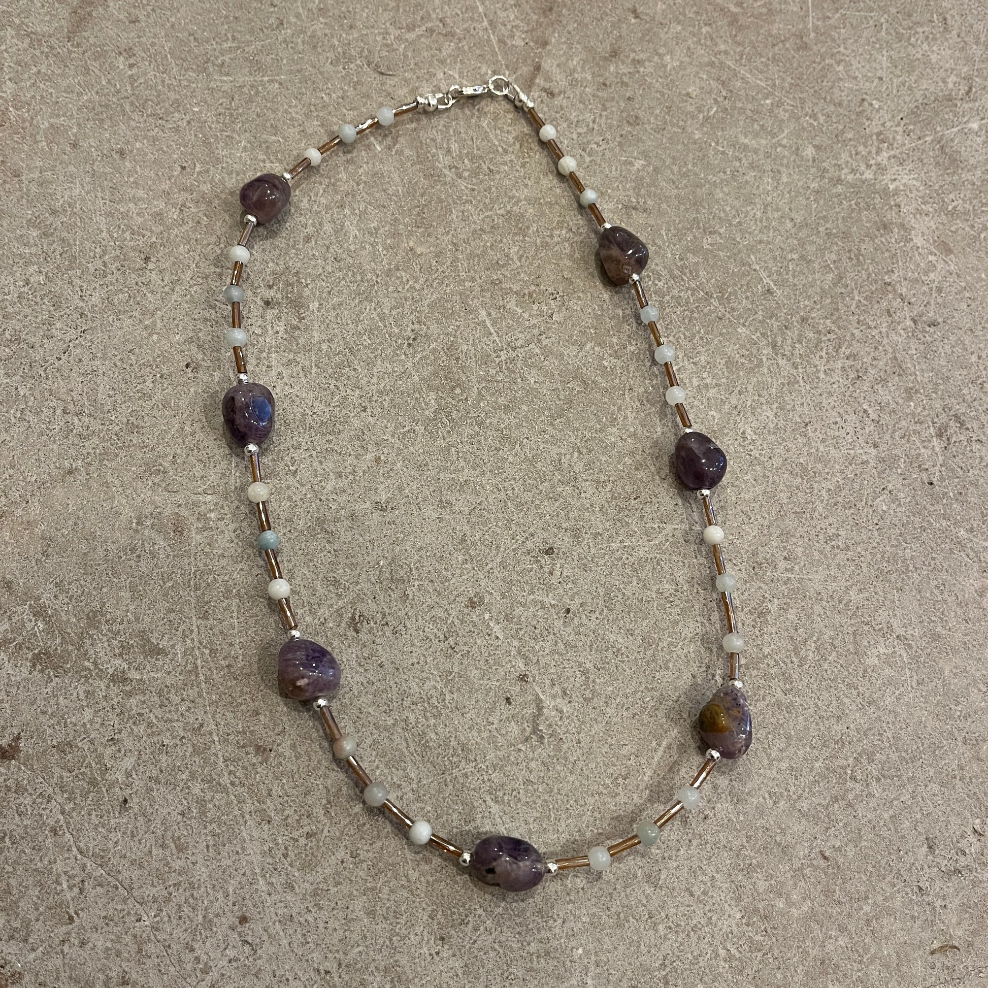 Necklace with purple and white beads on a concrete surface