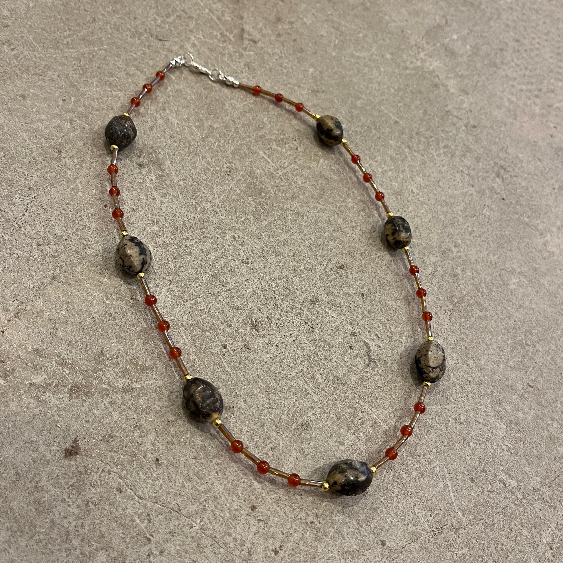 Necklace with dark beads and red accents on a concrete surface
