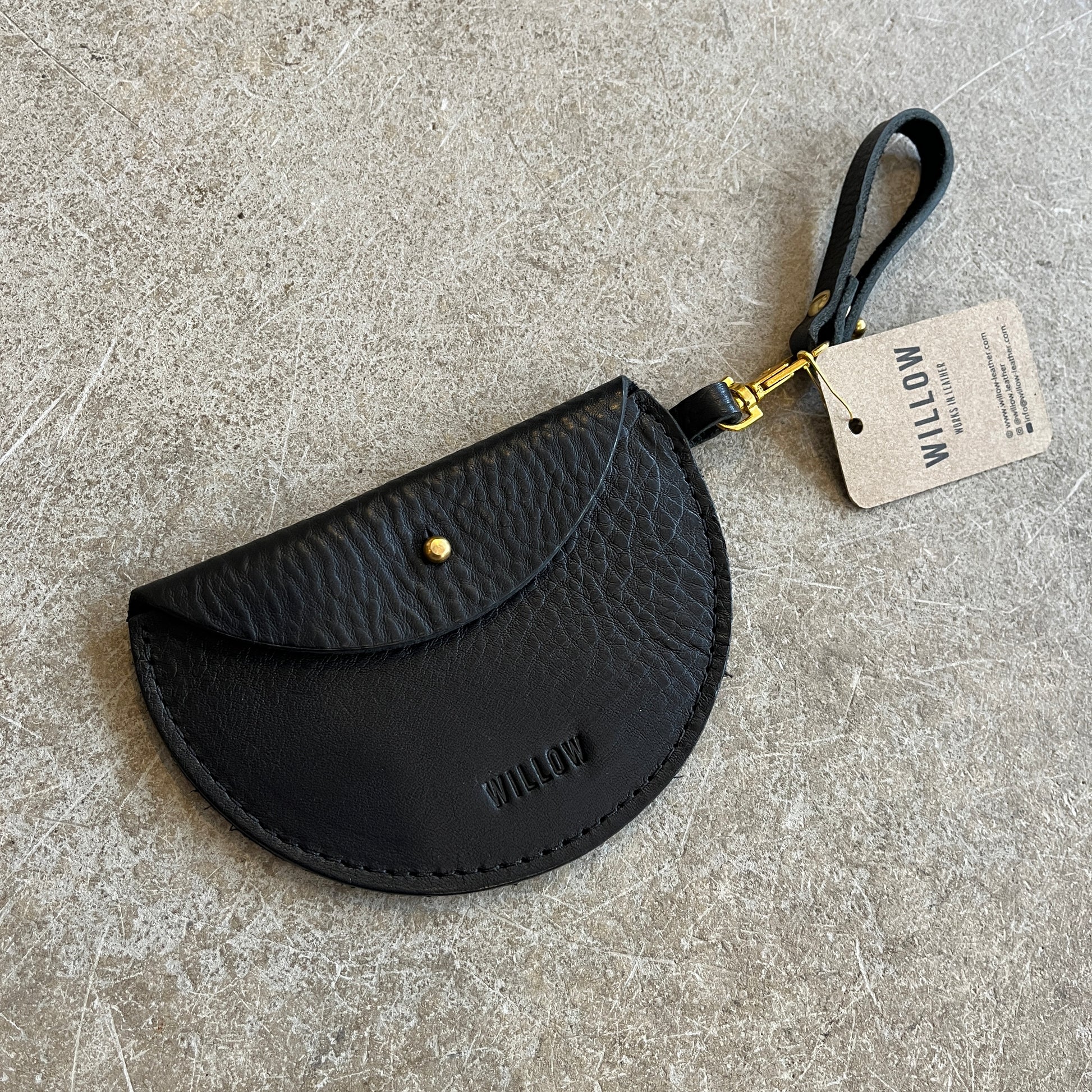 Three leather keyring purses in black, brown, and blue colors, displayed on a textured surface, each with a tag showing the brand name 'Willow Leather'.