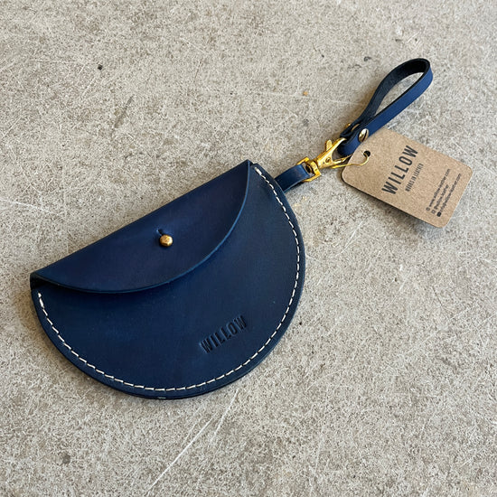 Three leather keyring purses in black, brown, and blue colors, displayed on a textured surface, each with a tag showing the brand name 'Willow Leather'.