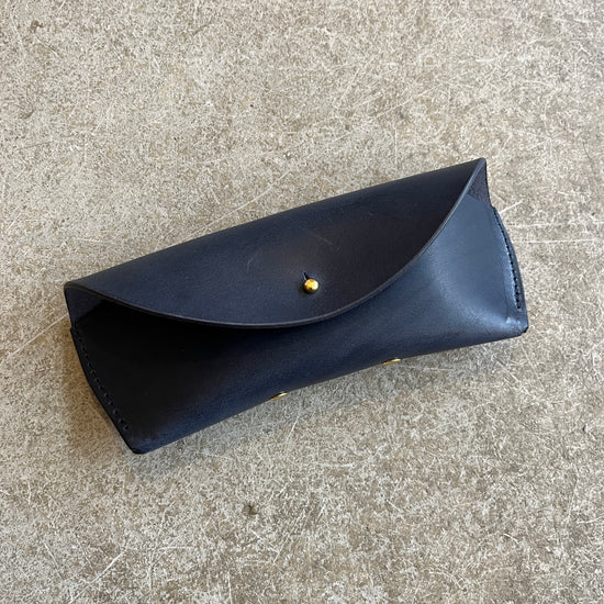 Four leather sunglasses cases in different colors (black, brown, tan) laid out on a textured surface.