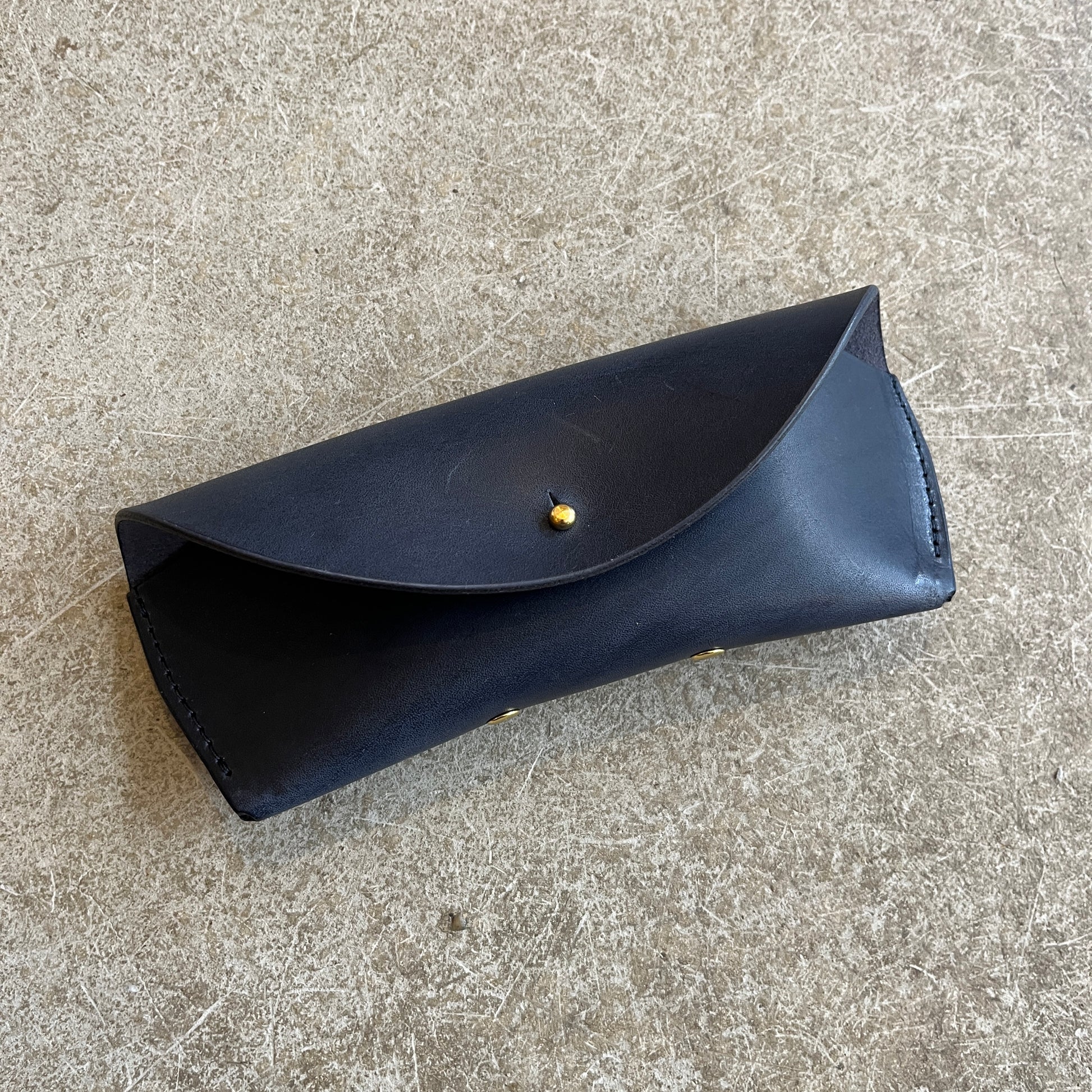 Four leather sunglasses cases in different colors (black, brown, tan) laid out on a textured surface.