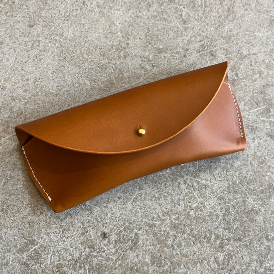 Four leather sunglasses cases in different colors (black, brown, tan) laid out on a textured surface.