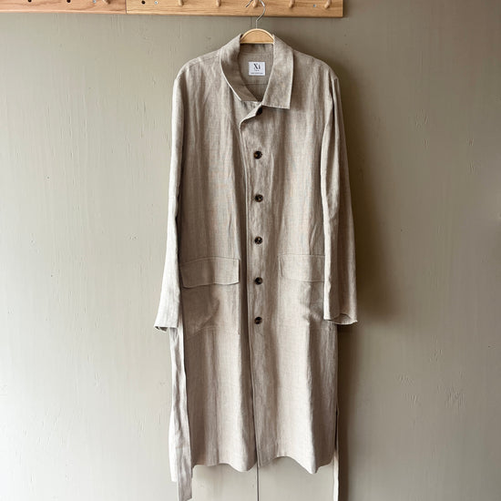 Beige coat hanging on a wooden hanger against a plain wall.