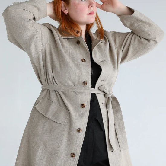 Woman wearing a beige trench coat with a plain background
