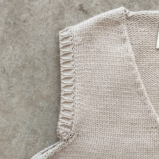 Close-up of a beige knitted sleeveless garment on a concrete surface