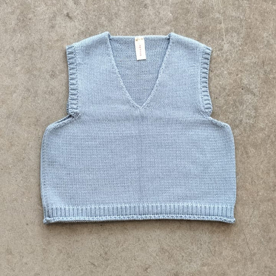 Light blue knitted vest on a beige surface