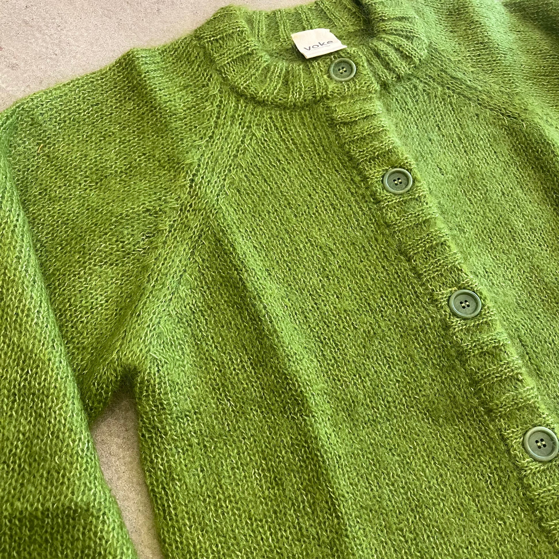 Green knitted cardigan with button details on a neutral background