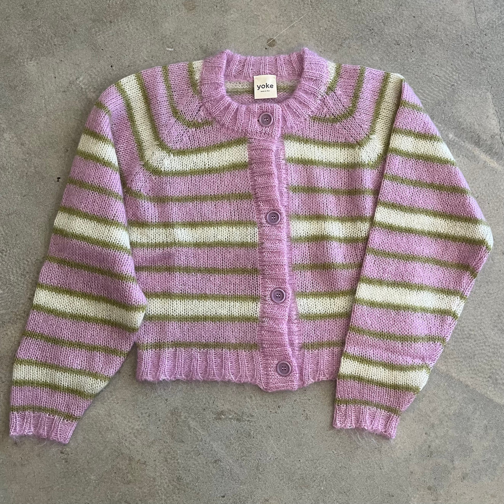 Striped cardigan with purple, green, and white colors on a gray surface