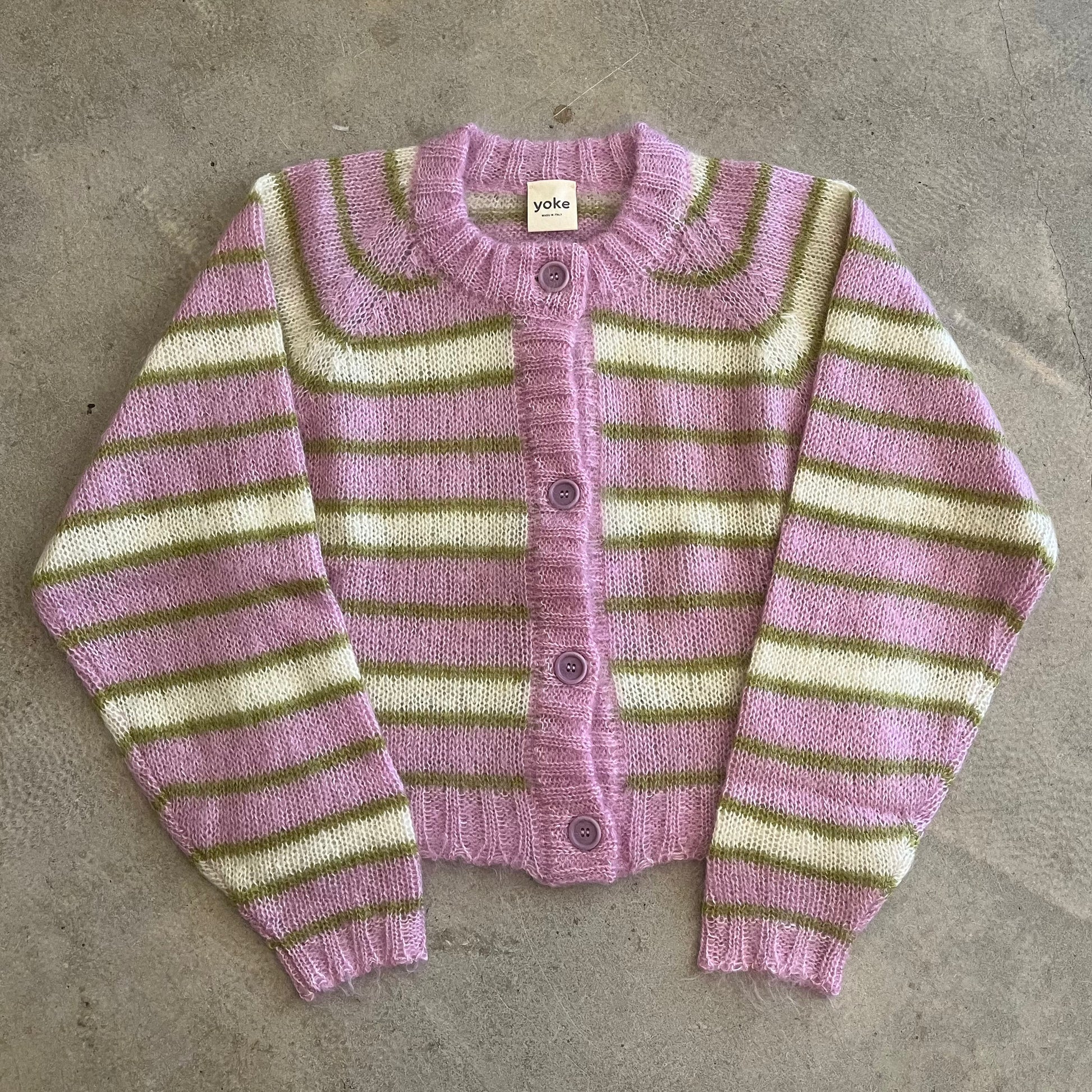 Striped cardigan with pink and green pattern on a concrete surface