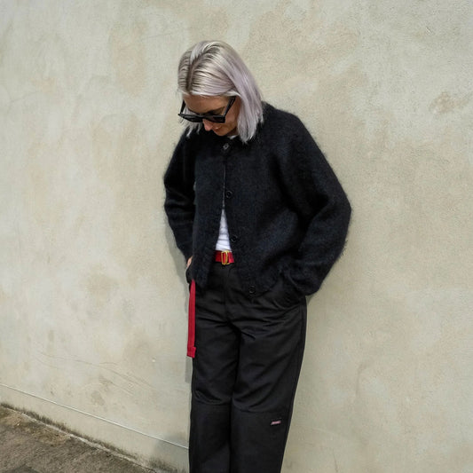 Woman leaning against a beige wall wearing a black cardigan