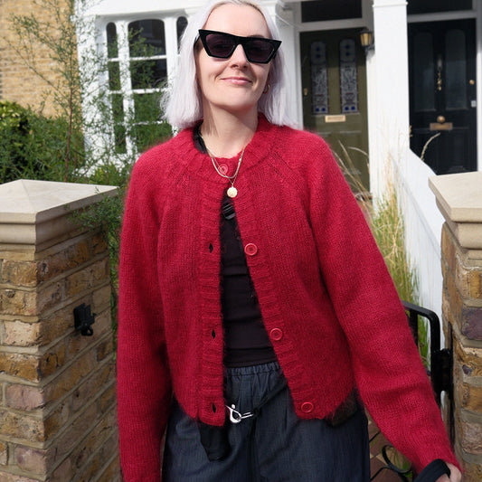 A woman stood outside a house wearing a red cardigan