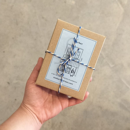 A hand holding a small box of greeting cards with a vegetable illustration on the cover, tied with a blue string.
