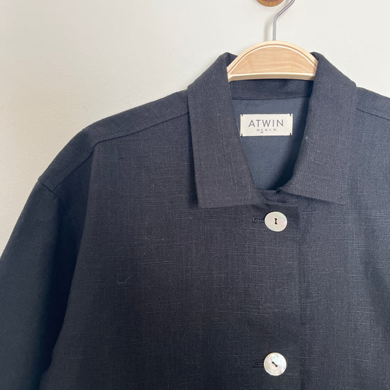black workwear jacket with 'ATWIN' label on a wooden hanger against a white background
